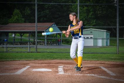 student hitting softball with bat at home plate